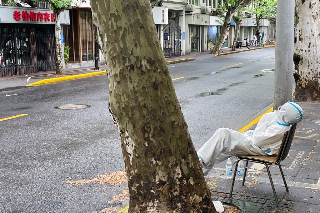 Ein müder medizinischer Mitarbeiter sitzt auf einer leeren Straße in Shanghai, China.