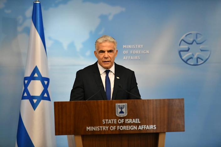 Der israelische Außenminister Yair Lapid auf einem Podest neben der israelischen Flagge, hinter ihm steht das Außenministerium auf der Wand.