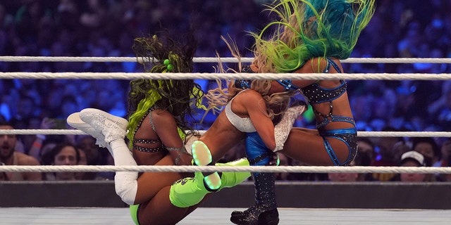 3. April 2022;  Arlington, Texas, USA;  Naomi (links) und Sasha Banks (rechts) greifen Carmella während eines tödlichen Vier-Wege-Matches in der Women's Tag Team Championship während WrestleMania in der AT&T Arena an  T.