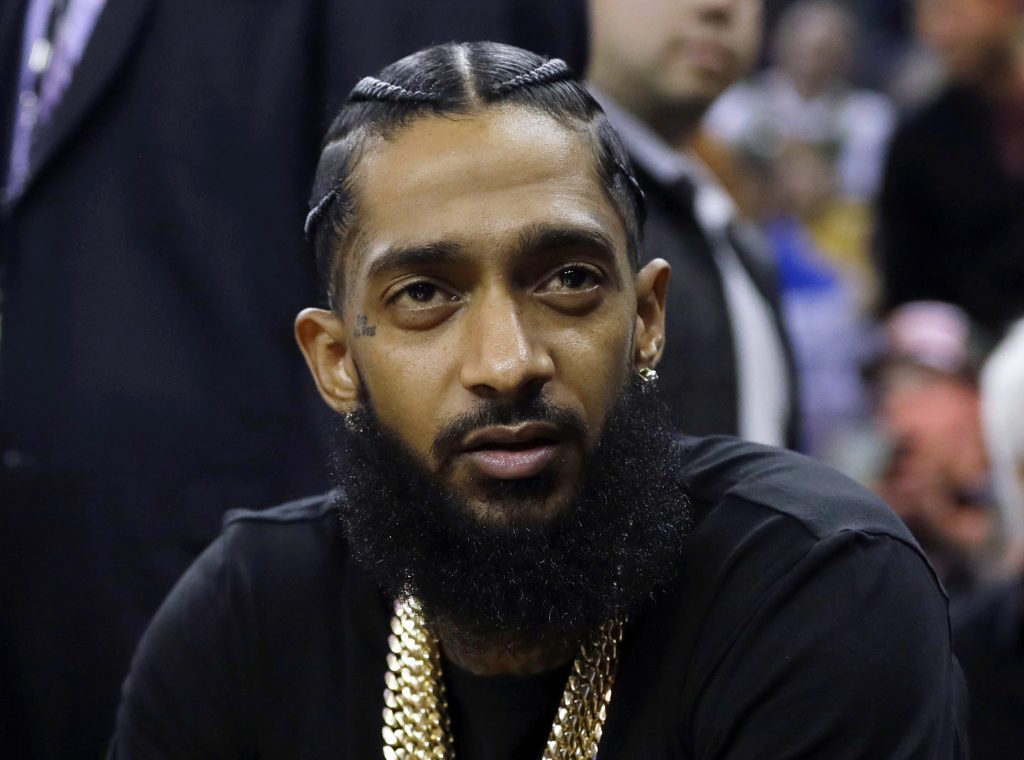 FILE - Rapper Nipsey Hussle attends an NBA basketball game between the Golden State Warriors and the Milwaukee Bucks in Oakland, Calif., March 29, 2018. Three years after rapper Hussle was gunned down outside a Los Angeles clothing store that he founded to help revitalize the neighborhood where he grew up, a trial will finally begin Wednesday, June 15, 2022, for the man charged with killing him. (AP Photo/Marcio Jose Sanchez, File)