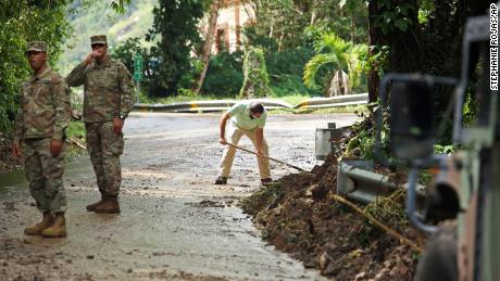 Die Nationalgarde erzwingt den direkten Verkehr, als der Einwohner Luis Nogueira am Dienstag in Cayai, Puerto Rico, hilft, eine vom Hurrikan Fiona beschädigte Straße zu räumen.